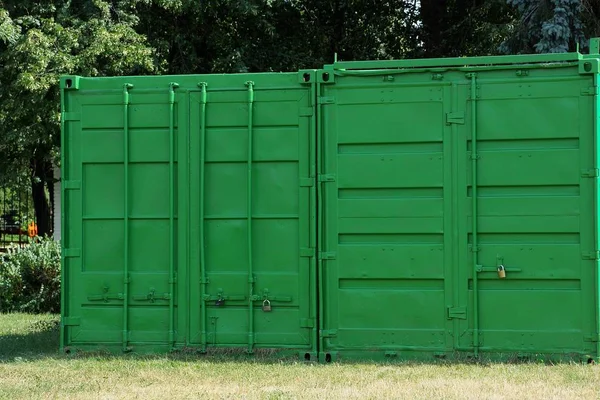 two green metal containers with a closed gate in the grass outside