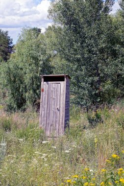 Çim ve ağaçlar arasında gri kırsal ahşap tuvalet
