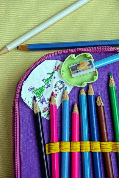 Colored pencils in a pencil case and a children`s drawing