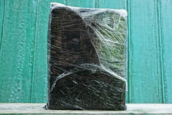 Černá Krabička Šedém Celofánu Stojí Stole Proti Zelené Stěně — Stock fotografie