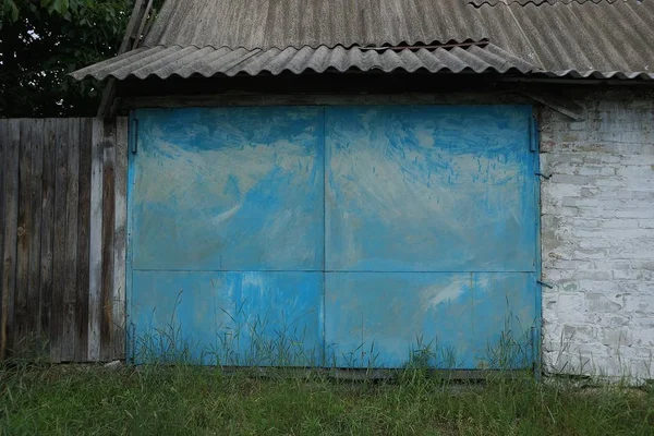 facade of an old garage with blue metal gates outside in green grass