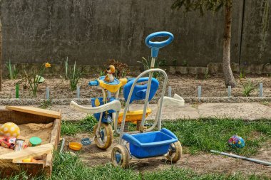 Çim ve kum havuzunda çocuk bisikleti ve oyuncaklar