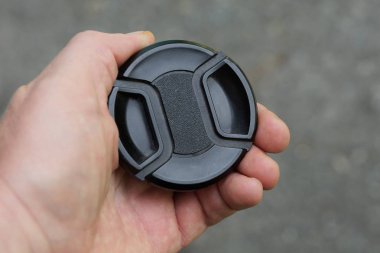 el sokakta gri bir arka plan üzerinde siyah plastik lens kapağı tutar