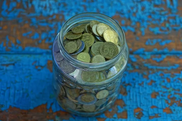 一个装满小硬币的玻璃罐站在一张蓝色的破旧桌子上 — 图库照片