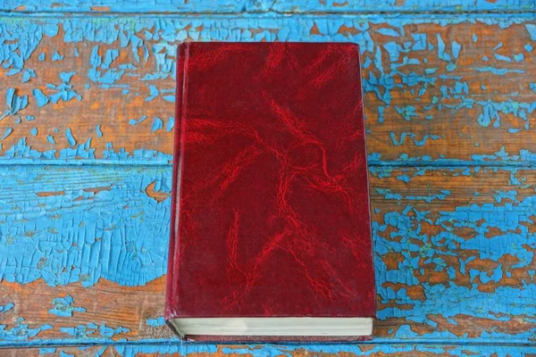 an old closed book with a red cover is lying on a blue brown worn table