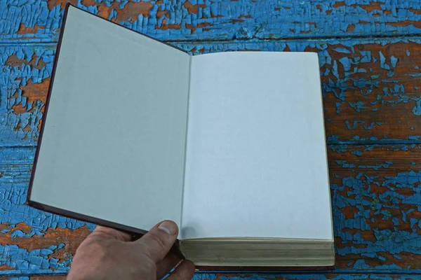 hand opens a book with white pages lying on a blue worn table