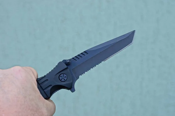 hand holds a black folding knife on a gray background