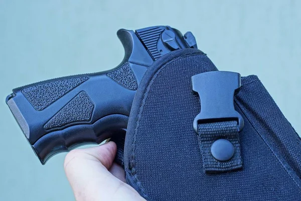 hand holds a black pistol in a holster on a gray background