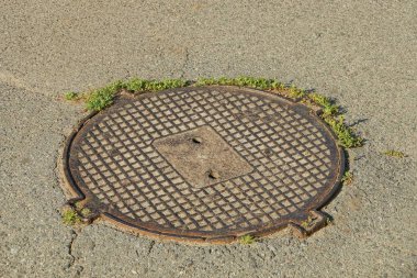 yeşil çim gri asfalt yolda eski kahverengi kanalizasyon rögar