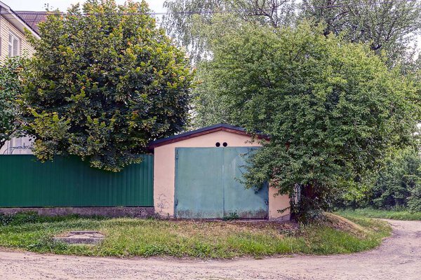 Гараж с железными зелеными воротами и забором вдоль дороги
