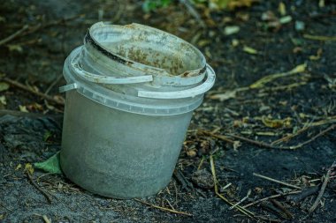 gri eski ve kirli plastik kova sokakta siyah zemin üzerinde duruyor