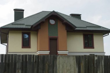 ahşap bir çit arkasında yeşil bir çatı altında pencereleri ile gri kahverengi ev