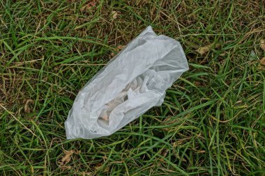 Beyaz boş plastik torbadan çıkan çöpler yeşil çimlerin üzerinde yatıyor. 