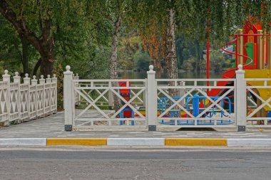 Yol kenarında ağaçlar olan bir oyun parkının önündeki beyaz çitin bir parçası.