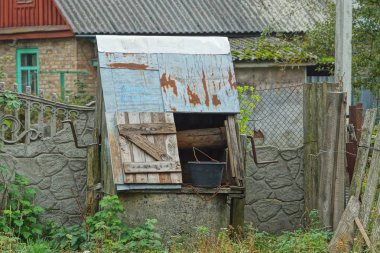 Yeşil çimlerde taş bir duvarın yanında bir kova ile açık gri eski kuyu