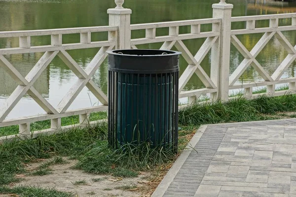 1つの黒い金属製の骨壷は貯水池の水の近くの岸の白い木製の柵のそばに立っています — ストック写真