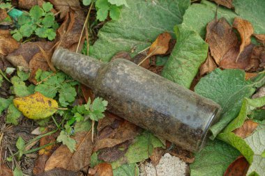 Doğadaki yeşil yaprakların üzerinde gri bir cam şişeden çıkan çöpler.