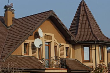 Mavi gökyüzüne bakan pencereli, büyük, özel bir evin çatısındaki kahverengi fayans.