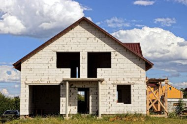 Gökyüzüne karşı boş pencereleri ve güneşli bir günde bulutları olan büyük, bitmemiş tuğladan özel bir ev.