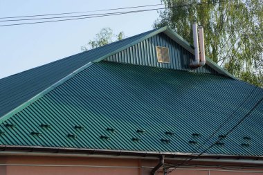 Gökyüzüne karşı yeşil metalin altında küçük bir penceresi olan özel bir evin tavan arası.