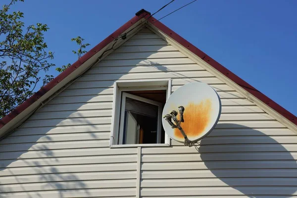 white plastic attic of a private house with one window and a satellite dish against a blue sky