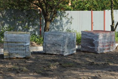 Üç kare kutu plastik ambalajda asfalt tuğlalar dışarıda gri zeminde duruyor.