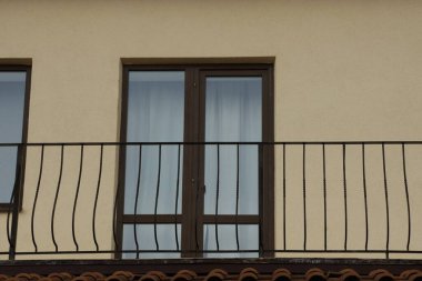 Siyah demir parmaklıklar açık metal bir balkonda, cam kapılı kahverengi bir duvara çarpıyor.