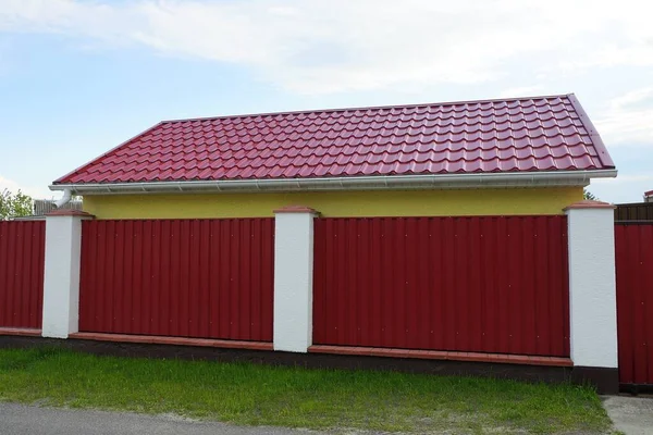red tile roof of a private house behind a metal fence against a blue sky