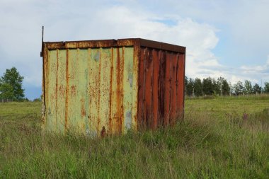 old yellow iron container in red rust stands in green grass