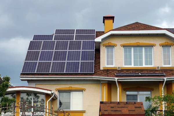 solar panels on the tiled roof of a large private house with windows on a background of gray sky with clouds