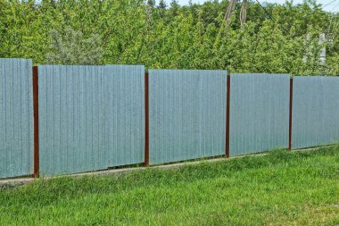 gray metal wall of a fence in the street in green grass and vegetation