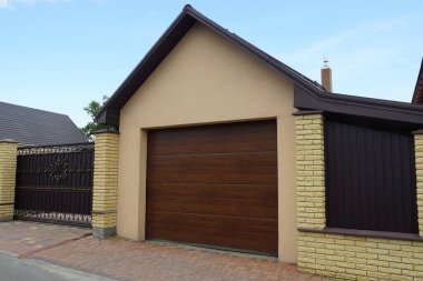 Kahverengi bir garajın ön cephesi ve sokakta metal kapıları olan bir çit.