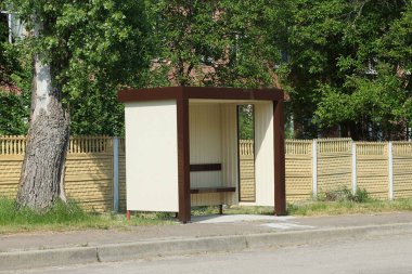 Sarı çitin önündeki yolda boş bir kahverengi plastik otobüs durağı.