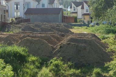 Yeşil bitki örtüsündeki bir inşaat alanında bir sıra gri toprak ve kahverengi kil.