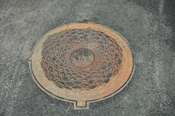 茶色の錆びた鉄の下水道マンホールが道路の灰色のアスファルトの上にあり — ストック写真