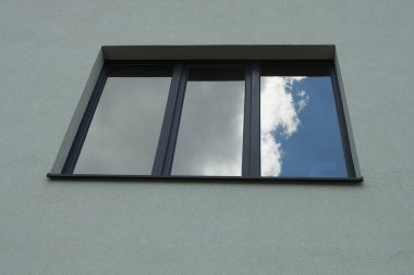 Binanın gri beton duvarında siyah büyük bir pencere var.