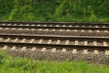Demiryolunun bir kısmı demiryolu ve küçük gri moloz yığınları ve yeşil çimlerle kaplı beton yataklı.