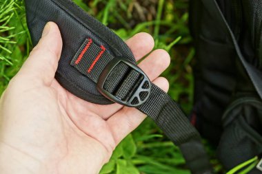 Doğadaki yeşil çimlerin arka planında elinde plastik bir karabinayla kumaştan yapılmış siyah kayış.