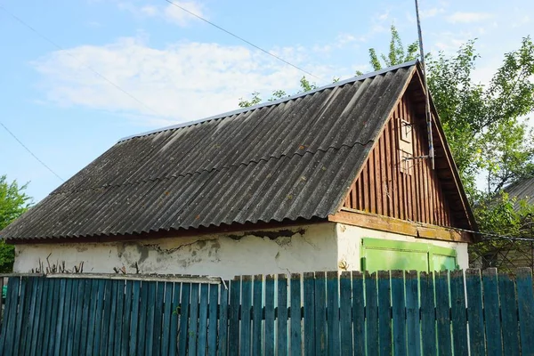 old rural barn with gray slate roof behind a wooden fence against the sky