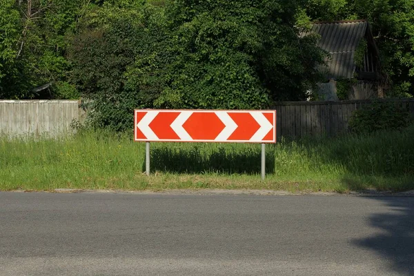 一个路标在柏油路旁边的绿草中 用红色箭头指示转弯方向 — 图库照片
