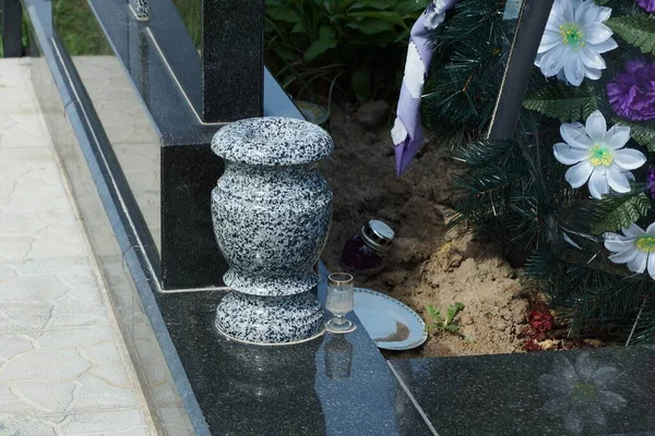 one empty gray stone vase stands on a black marble slab of a grave in a cemetery