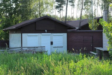 Pencerelerinde ve kapılarında beyaz panjurlar olan gri özel bir ev. Kahverengi bir çatısı ve yeşil çimlerin üzerinde tahta bir çit var.