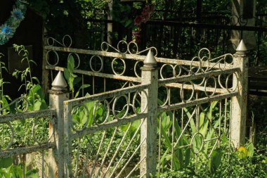 Mezarlıktaki mezarlıkta yeşil çimlerle kaplanmış demir parmaklıklardan yapılmış gri, eski metal bir çitin parçası.