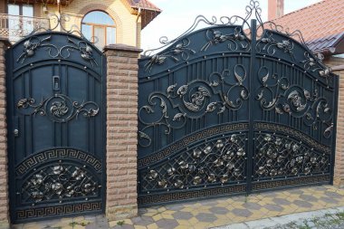 Siyah demir kapı ve kapı işlemeli demir desenli ve kaldırımdaki duvarda kahverengi tuğlalar