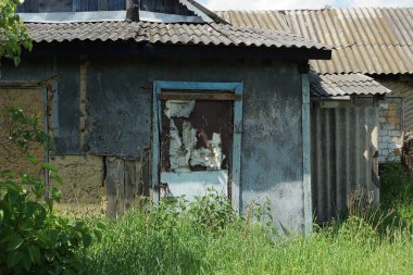 Terk edilmiş bir kırsal evin gri duvarında yeşil çimen ve bitki örtüsüyle kaplanmış eski püskü bir kapı.