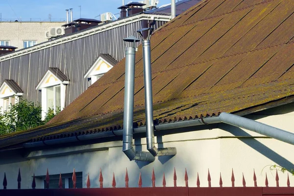 靠近棕色石板屋顶的房子墙上有两条灰色金属烟囱 — 图库照片