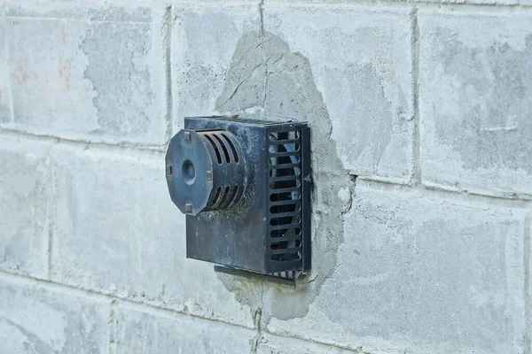 one black iron hood with a fan on a gray brick wall of a building outside