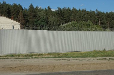 Uzun, gri, dikenli telli çit duvarlı, yolun yanındaki yeşil çimlerde.