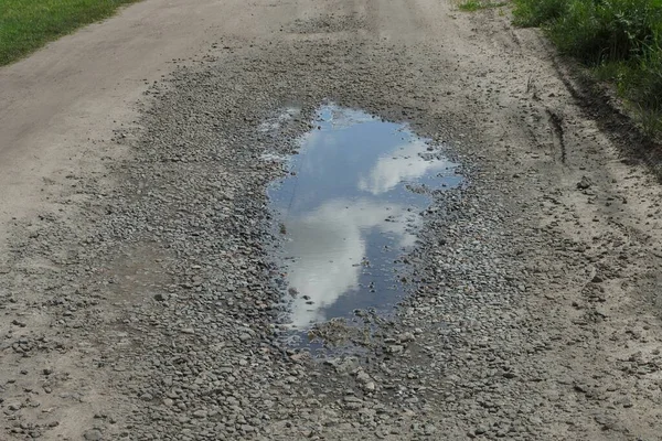 one big puddle on the road in gray earth and small  rubble