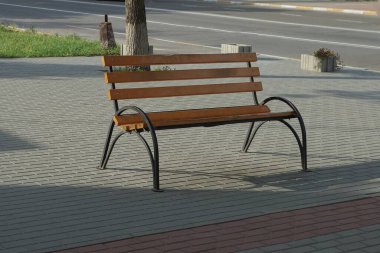 Tahtalardan ve siyah demirden yapılmış kahverengi boş bir bank sokağın gri kaldırımında duruyor.